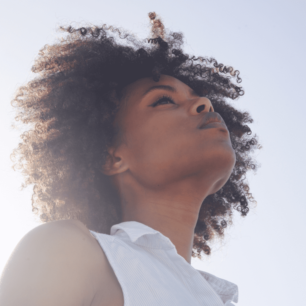 Profile of young black woman with curly natural hair looking towards the sky.